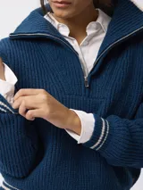 Sweater de tejido grueso en color beige, con cuello alto y cierre frontal parcial. Presenta detalles de rayas negras en contraste en el borde del cuello y en los puños.