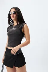 Remera sin mangas, ajustada al cuerpo, color gris oscuro o negro gastado, con cuello redondo y terminaciones de volados en las sisas. Estampado frontal con texto en blanco que dice "*rea ess*" y "*fearless*".