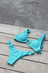 Bikini color turquesa con textura acanalada. El top tiene triángulos fijos unidos por una argolla, breteles regulables y lazo en la espalda. El bottom es vedetina con argollas en la cadera.