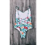 Malla enteriza blanca con estampado de hojas y flores en tonos celeste, verde, naranja y rojo. Espalda con tiras cruzadas.