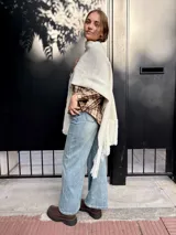 Ruana tejida de lana en color crudo, con diseño de flecos en los bordes. Es una prenda versátil y abrigada, ideal para complementar diversos looks.