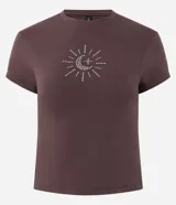 Remera baby tee de algodón color marrón oscuro, con cuello redondo, manga corta y calce ajustado. Presenta un aplique frontal de pedrería brillante con diseño místico de sol, luna y estrella.