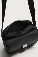Bandolera de acabado engomado negro con compartimento principal con cierre, bolsillo interior con cierre y bolsillo frontal con solapa y hebilla metálica de liberación rápida. Cuenta con asa de hombro ajustable y extraíble.