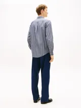 Camisa Tommy Hilfiger de corte regular, confeccionada en popelín de algodón azul con rayas verticales texturizadas. Presenta cuello camisero, cierre frontal de botones, mangas largas con puños abotonados y logo bordado en el pecho.