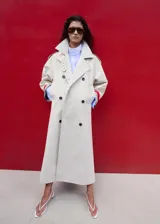 Chaqueta larga de algodón color beige, de diseño recto con cuello en pico y solapas con muesca. Cuenta con cierre delantero de doble botonadura, bolsillos laterales y mangas largas reversibles.