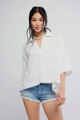 Blusa blanca de algodón vaporoso, con diseño holgado y ligeramente extragrande, cuello camisero, cierre frontal de botones y mangas amplias.