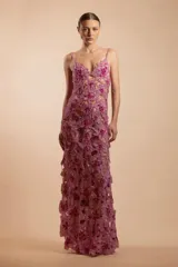 Vestido largo de fiesta con diseño de encaje calado y bordados florales en tonos fucsia y violeta. Presenta escote en V, breteles finos y una silueta ajustada que se extiende hasta los pies con una caída fluida.
