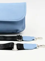 Bolso pequeño tipo bandolera o riñonera, color celeste claro, con solapa frontal y correa ancha ajustable de color negro con herrajes metálicos.