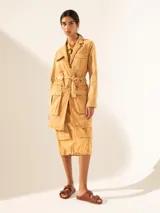 Tapado color ocre con cuello camisero, cierre frontal con botones y cinturón de la misma tela. Tiene múltiples bolsillos con solapa y botón en el frente.
