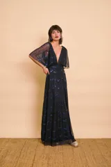 Vestido largo negro con brillos azules, escote en V pronunciado, mangas cortas y amplias tipo capa, y corte en la cintura.