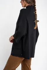 Cardigan negro de corte oversize, con cuello alto, cierre frontal de botones y mangas tres cuartos. Presenta un diseño holgado con bolsillos frontales y una caída fluida.