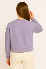 Buzo de cuello redondo en color lila, con detalle de costura en forma de X en el pecho, mangas largas con puños elásticos y corte cropped.