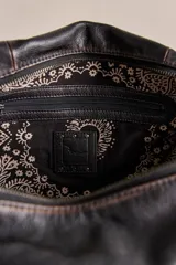 Bolso tote de cuero lavado negro con efecto gastado, interior amplio, bolsillos exteriores con cremallera, dos asas de mano y correa desmontable y regulable.