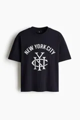 Remera de algodón color negro con cuello redondo acanalado, mangas cortas y hombros caídos. Presenta un estampado frontal en color blanco con la inscripción New York City y un monograma central.