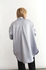 Camisa celeste de seda sintética, corte holgado, mangas largas abullonadas con puños elásticos y bolsillos laterales.