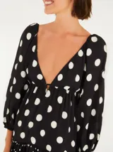 Vestido corto con estampado de lunares blancos sobre fondo negro, con escote profundo en V, mangas largas abullonadas y falda en capas con acabado en marias.