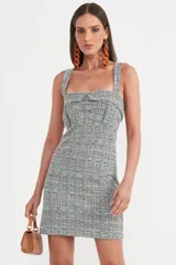 Vestido corto de tweed con estampado a cuadros en tonos gris, celeste y blanco. Tiene breteles anchos, escote cuadrado y corte ajustado.