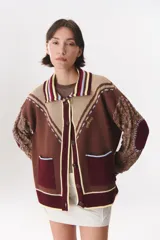 Cardigan de punto con diseño multicolor en tonos marrón, bordó y crema. Presenta cuello tipo polo, cierre frontal con botones, bolsillos aplicados en el frente y mangas con trama trenzada y coderas. Incluye detalles bordados y costuras decorativas.