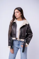 Campera tipo gamulán de cuero sintético marrón oscuro con interior y detalles de corderito sintético en cuello y puños. Presenta cierre frontal, bolsillos laterales con cierre y correas ajustables en el cuello.