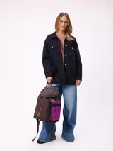 Mochila urbana marca Rusty de color negro, con múltiples compartimentos frontales, bolsillo de red lateral y detalles en azul y amarillo. Presenta el logo de la marca en la solapa superior y el texto 'Rusty Worldwide' en el frente.