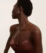 Conjunto de collar y caravanas dorados. El collar es tipo gravata con una cadena fina y un colgante de esfera roja. Los aros son aros pequeños con forma orgánica.