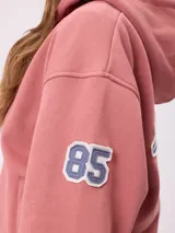 Canguro azul marino con cierre frontal, capucha y bolsillos laterales. Presenta un parche bordado con el número 85 en color celeste y blanco en la manga.