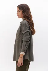 Camisa beige de manga larga, con cuello clásico, botones marrones y dos bolsillos frontales. Presenta costuras decorativas en contraste.