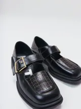 Zapatos tipo guillermina con punta cuadrada, confeccionados en lona resistente con estampado de cuadros escoceses en tonos beige, rojo y negro. Presentan una correa ajustable con hebilla metálica color bronce y una suela con taco de 4 cm.