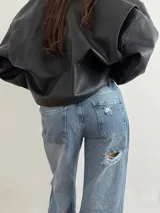 Pantalón de jean estilo wide leg con diseño de cintura cruzada y tiro bajo. Presenta un lavado azul medio con efecto desgastado y un detalle de rotura en la rodilla derecha.