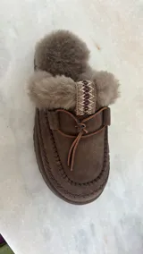 Pantuflas UGG de cuero color marrón con interior de piel sintética y detalle de costuras en contraste.