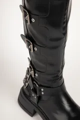 Bota de caña alta color negro, con suela track y múltiples hebillas metálicas.