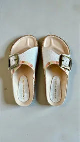 Sandalias Carolina de Cunto modelo Kira de la línea Ottenta, color blanco con detalles artísticos en tonos rosados y tostados. Presentan una tira ancha con hebilla metálica grande y plantilla anatómica.