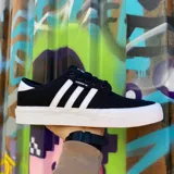 Championes Adidas modelo Seeley XT, de diseño urbano y estilo skate. Presentan una capellada de lona negra con las icónicas tres tiras laterales en color blanco, suela de goma vulcanizada blanca y cierre de cordones.