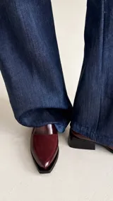 Bota corta de cuero con textura tipo reptil y paneles de gamuza en tono marrón oscuro. Presenta un diseño de punta cuadrada, cierre lateral y un taco cuadrado de madera.