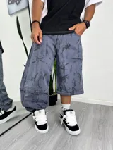 Pantalón ancho estilo baggy, color azul grisáceo, con estampado abstracto en negro. Presenta un diseño desmontable que permite convertirlo en un pantalón corto o bermuda, con cierres a la altura de la rodilla.