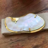 Cinturón de cuero color tostado con hebilla grande irregular de nácar con borde dorado.