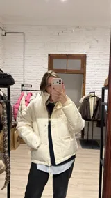 Campera tipo puffer color crema, con cuello alto, cierre frontal con botones a presión y bolsillos laterales con cierre.