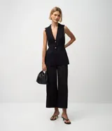 Pantalón pantacourt negro de sastre, con cintura alta, cierre interno discreto y pliegues delanteros sutiles.