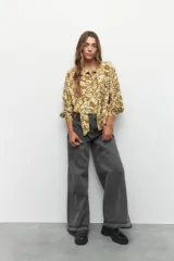 Camisa blanca con estampado floral en color marrón, de manga larga con puños abotonados, cuello con lazo y cierre frontal con botones.