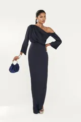 Vestido largo color azul marino, con escote asimétrico de un solo hombro y manga larga acampanada. El cuerpo superior presenta drapeado y la falda es ajustada y recta.