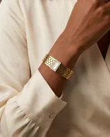 Esclava rígida de acero con baño de oro, con diseño de malla hexagonal calada. Presenta un aplique central rectangular con incrustaciones de circonias y centro de nácar.