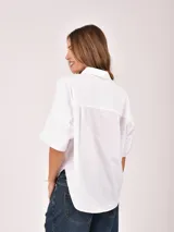 Blusa blanca de manga corta, con cuello camisero y abertura frontal parcial con botones. Presenta un corte holgado y bajo redondeado.