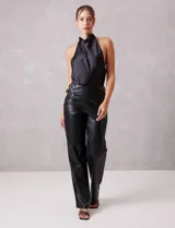 Pantalón de cuero sintético negro, de corte recto y tiro alto. Presenta cintura con hebillas laterales regulables y cierre frontal.