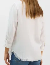 Camisa de tencel color blanco, con cuello camisero, cierre frontal de botones y dos bolsillos en el pecho. Presenta mangas largas con presilla para regular el largo y ruedo con detalle de flecos.