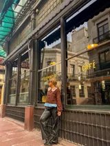 Camisa de color marrón con cuello Peter Pan en tono beige con borde de encaje, mangas largas abullonadas con puños elásticos y detalle de volado en el ruedo en color celeste.