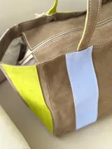 Bolso tipo shopper de diseño amplio, confeccionado en gamuza con un patrón de franjas verticales en tonos marrón oscuro, rosa y verde oliva. Cuenta con doble asa de hombro y cierre superior.
