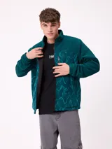 Campera reversible con cuello alto y cierre frontal. Un lado presenta tejido de polar con estampado geométrico en tonos verdes y bolsillo con cierre en el pecho, mientras que el otro lado es de nylon. Cuenta con puños elásticos y bolsillos laterales.