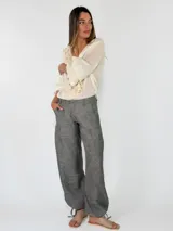 Pantalón de lino color beige, de corte holgado tipo jogger con puños ajustables con cintas en los tobillos, bolsillos laterales y cierre frontal con botón y cremallera.