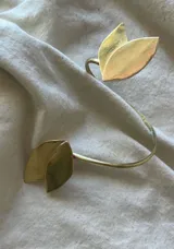 Brazalete abierto de metal dorado con apliques de hojas.