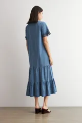 Vestido midi de jean azul, de corte holgado y diseño en capas con volados, escote en V, mangas cortas con detalles bordados en los puños.